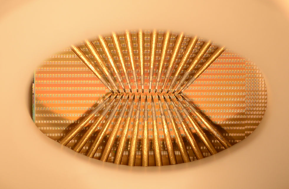 A photo of a wafer full of phase-change devices (the silver squares). The probe needles are required to make the actual thing work: this is a prototype chip without the usual traces/pins that would connect it to a circuit board. 
