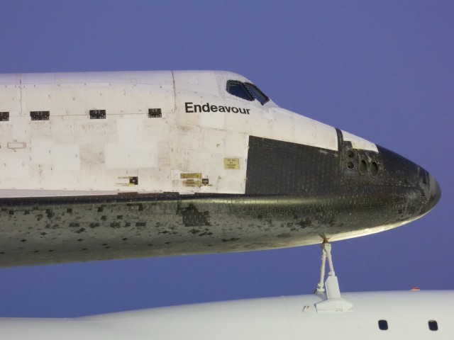 Close view of Endeavour's forward section and flight deck. At full magnification, the caution decals are readable. Each black TPS tile is individually numbered; the numbers are visible but illegible at this distance.