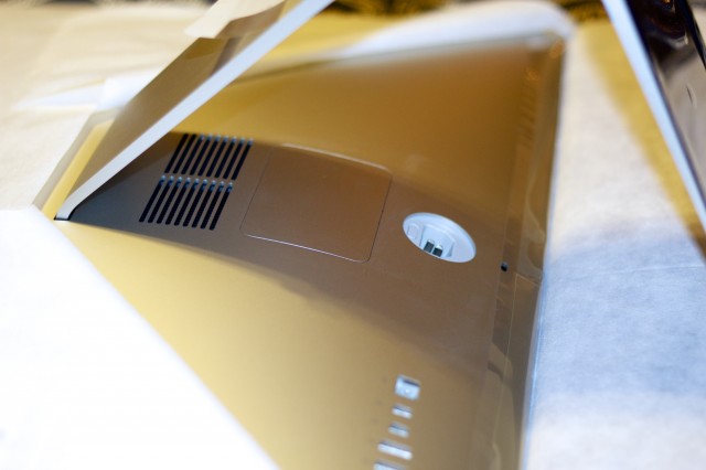 The rear of the iMac shows the RAM door. The button to open the hatch is visible at the top edge of the power socket.