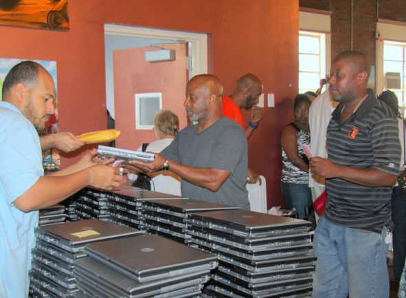 At Digit All Systems' "Stop Shooting, Start Coding" event on July 15, a member of DAS' staff distributes laptops to people who have turned in firearms to police.