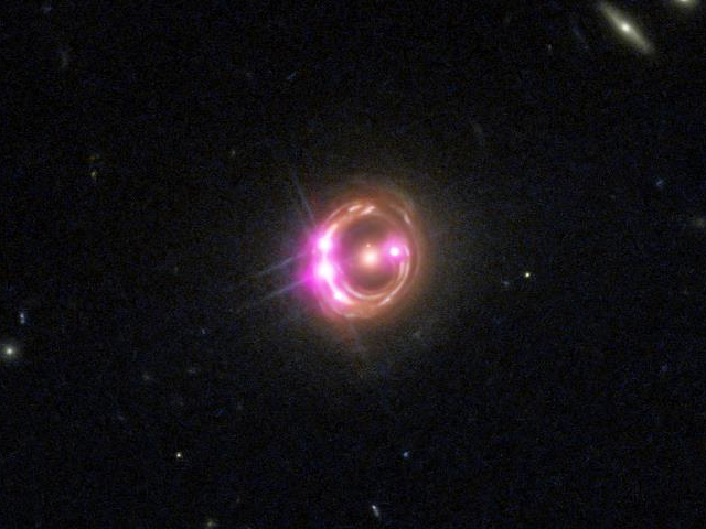 The four bright magenta points are images of a single quasar, magnified and multiplied by the gravity of the galaxy (colored orange) at image center.