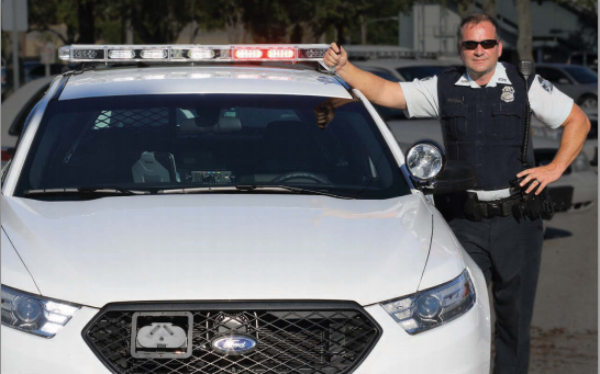 An officer posing next to cruiser equipped with the Starchase pursuit management system. 