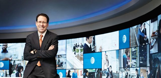 AT&T CEO Randall Stephenson standing with arms crossed in front of a backdrop with AT&T logos.