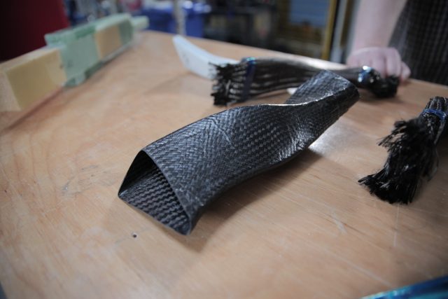 A finished model turbine component made from carbon fiber composite, with non-epoxied carbon fiber thread forms in the background.