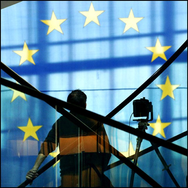 The silhouette of a photographer and his camera are shown against an EU flag.