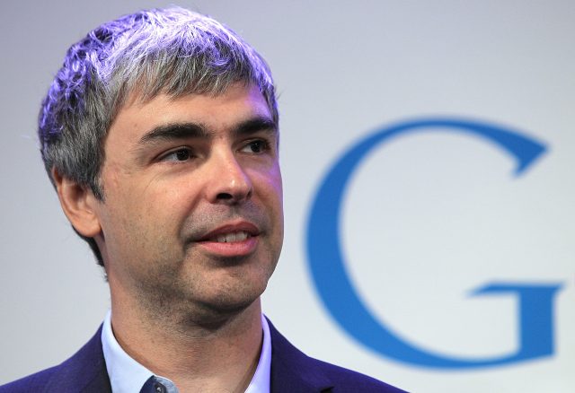 A man in an open-collar suit stands in front of a Google logo.