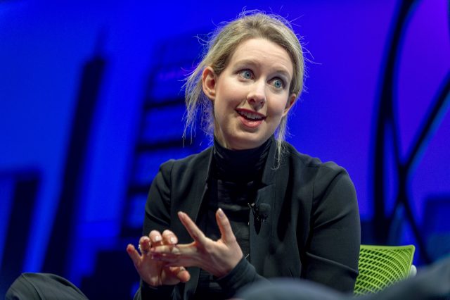 A woman dressed in black gestures while speaking.