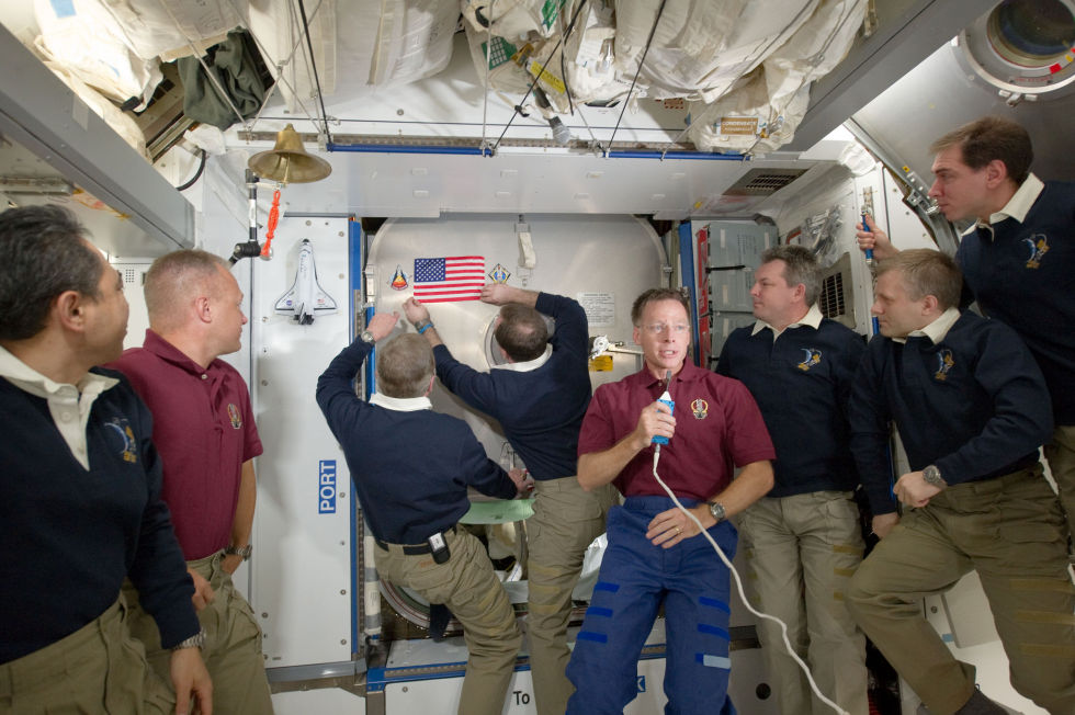 Mike Fossum and Ron Garan hang an American flag at the station during a ceremony, while Chris Ferguson says a few words.