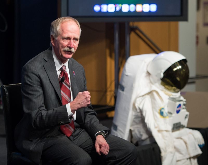 A man in a business suit stands next to a display spacesuit.