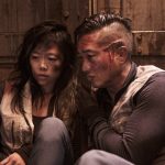 Two injured, dirty people cower somewhere futuristic.