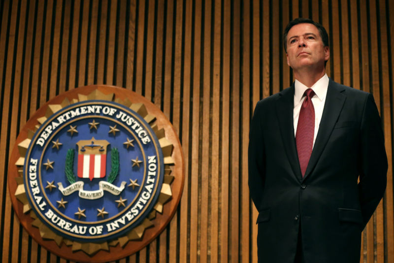 Then-FBI Director James Comey stands in front of a FBI wall sign.