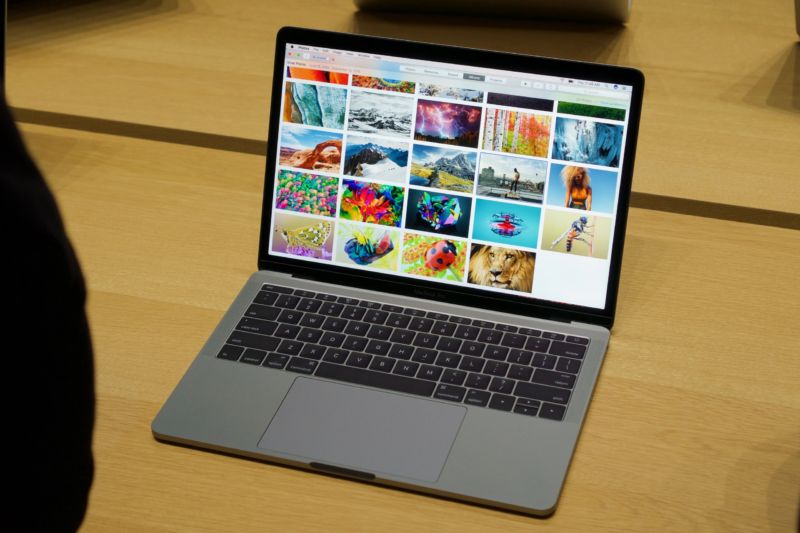 MacBook Pro without TouchBar, sitting on a wooden table, showing photos on its screen.