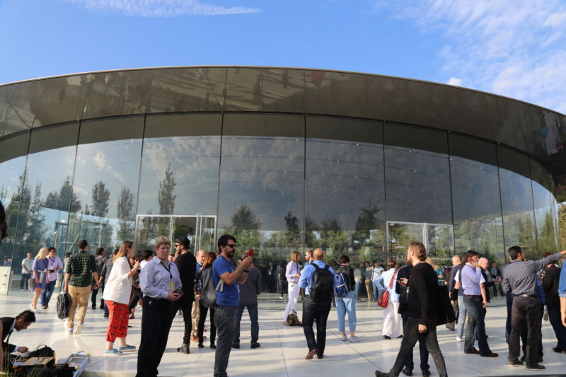 People cluster outside a futuristic glass-and-steel building.