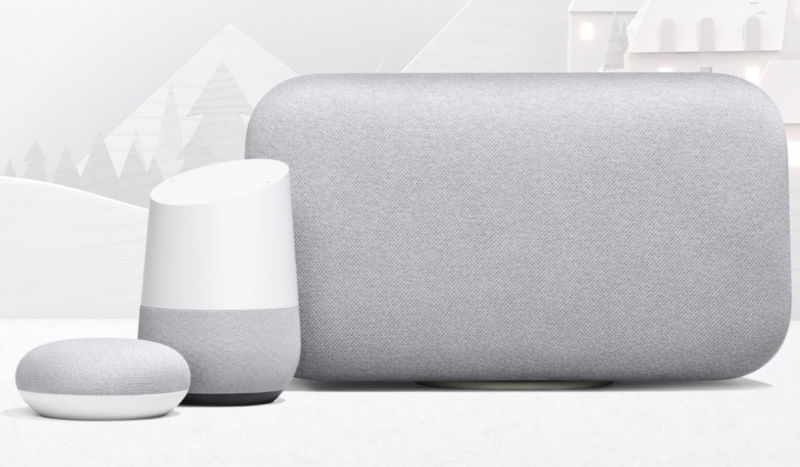 Three different Google Home smart speakers sit one next to each other on a table.