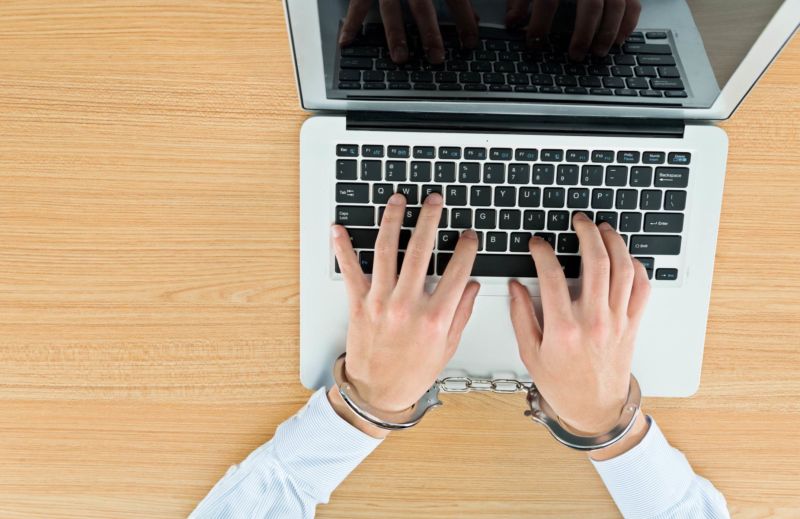 A man's hands typing on a laptop while handcuffed.