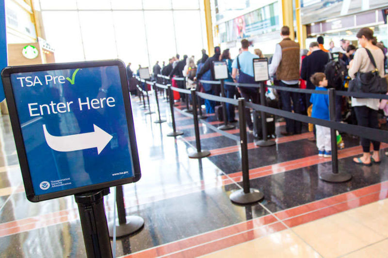 People waiting in an airport security line, with an empty line for TSA Precheck.