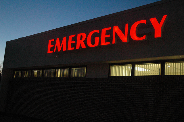 A neon emergency sign on the outside of a hospital at night