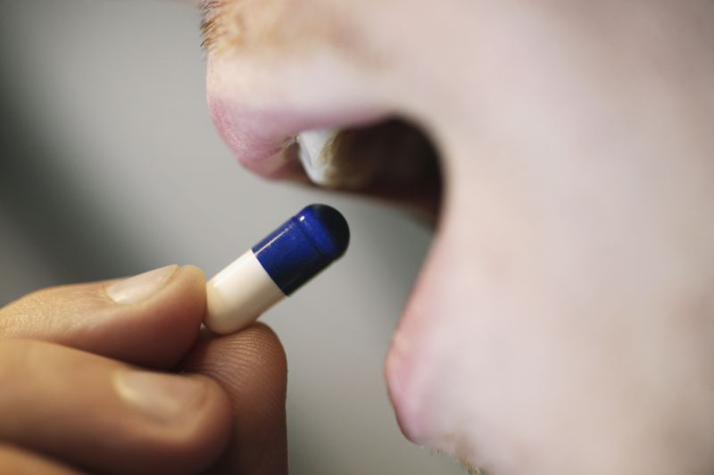 Close-up of person putting blue and white tablet in mouth