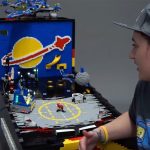 A woman next to a pinball machine made entirely from LEGO bricks.