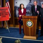 Three Democratic senators speaking next to a sign that says, "One more vote to save net neutrality. We will force a vote."