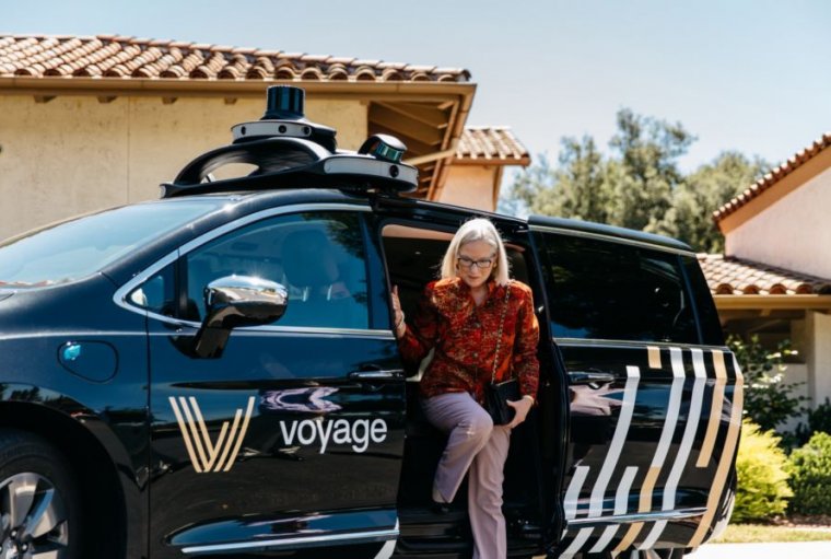 A silver-haired woman steps from a self-driving minivan.