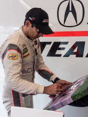 Helio Castroneves signs a fan's photo of his Acura race car
