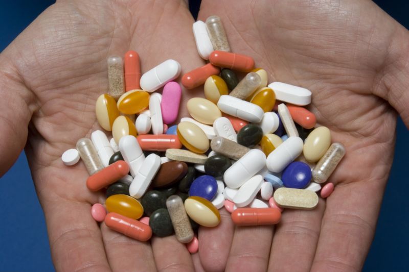 A close-up of hands holding a large assortment of pills.