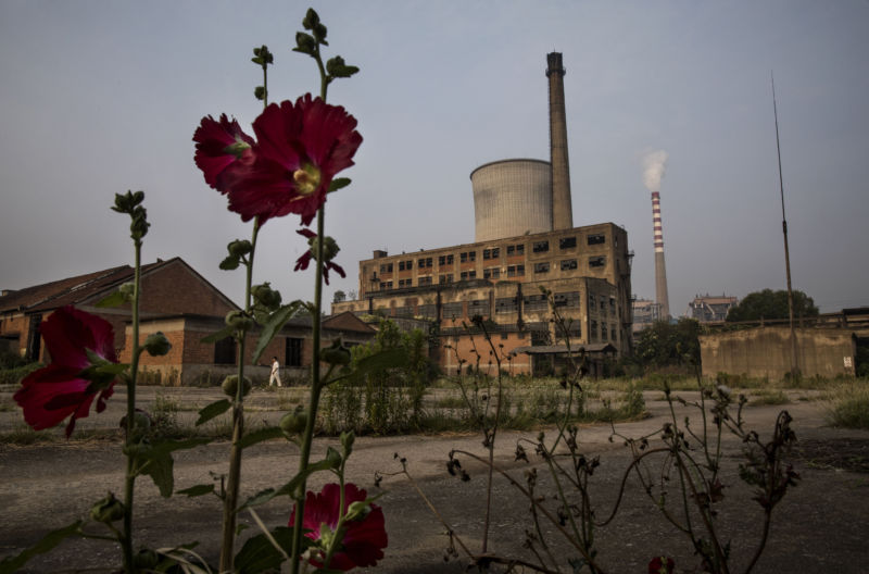HUAINAN, CHINA - JUNE 16: A smokestack from a coal fired power plant is seen next to an abandoned former paper factory near the site of a large floating solar farm project under construction by the Sungrow Power Supply Company on a lake caused by a collapsed and flooded coal mine on June 16, 2017 in Huainan, Anhui province, China. (Photo by Kevin Frayer/Getty Images)
