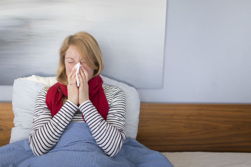 A sick woman sits in bed and blows her nose.