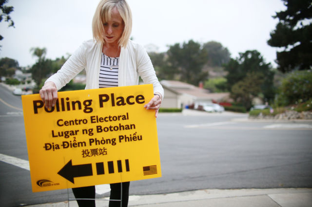 Volunteer Janice MacGurn sets up a polling station sign before opening on primary election day June 5, 2018 in San Diego, California. There are several highly competitive races throughout the state including those for governor and U.S. House and Senate seats.