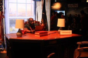 A man sits at a faux oval office desk