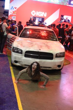 A zombie woman pretends to be trapped under a rusty car