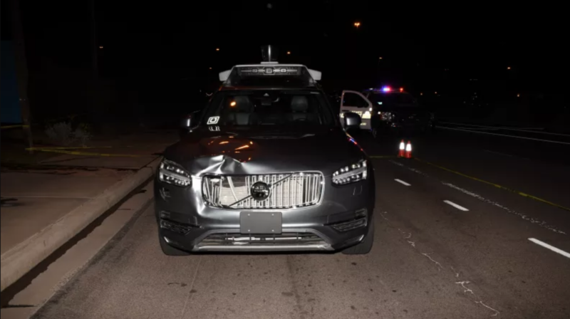 A silver SUV with a damage grill is parked on a street at night.