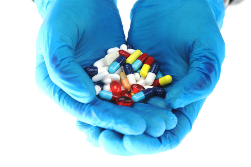 Hands wearing blue surgical gloves hold brightly colored medications, including antibiotics.
