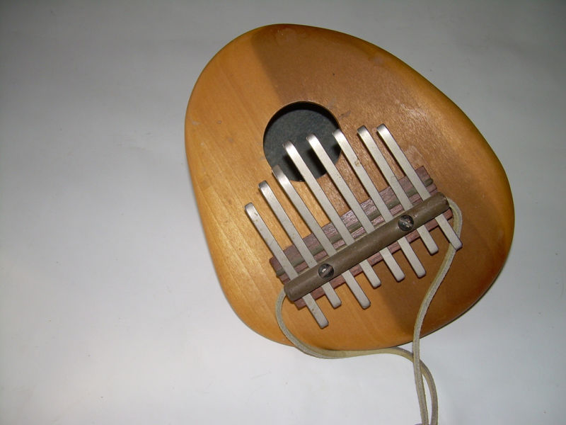 An Mbira: a musical instrument consisting of a wooden sound box with a series of metal teeth that hang over the hole in the sound box.