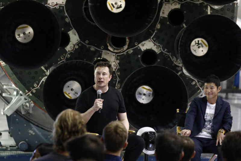 Elon Musk vorbește în timp ce Yusaku Maezawa, fondatorul și președintele Start Today Co., urmărește un eveniment la sediul SpaceX din Hawthorne, California, în 2018.