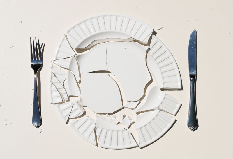 Broken plate with knife and fork on white background.