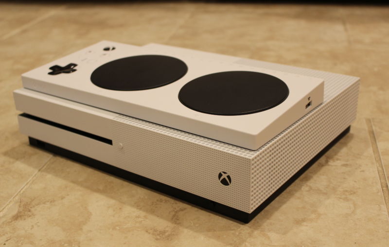The brand-new Xbox Adaptive Controller, posing on top of its black-on-white gaming sibling, the Xbox One S console.