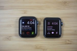 The case of an Apple Watch Series 4 next to a case of the Apple Watch Series 3 on a wooden table.