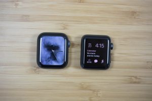 The case of an Apple Watch Series 4 next to a case of the Apple Watch Series 3 on a wooden table.