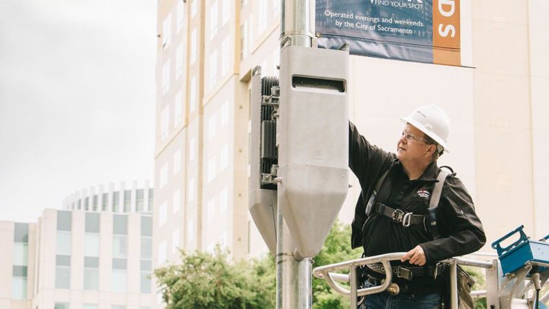 A Verizon construction engineer inspects a pair of radio heads on a mock small cell attached to a pole.