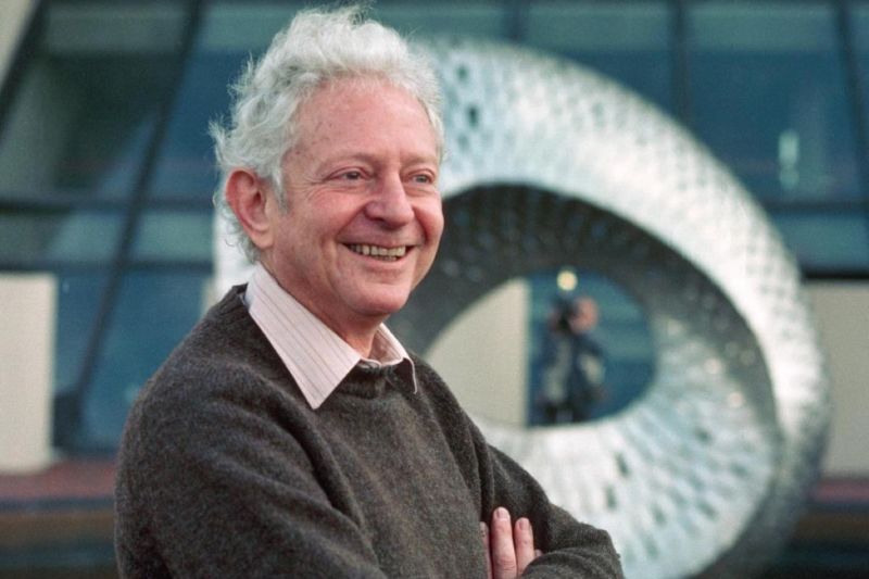 A smiling white-haired man in a sweater.