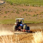 Image of a tractor sending dust into the air while plowing a field.