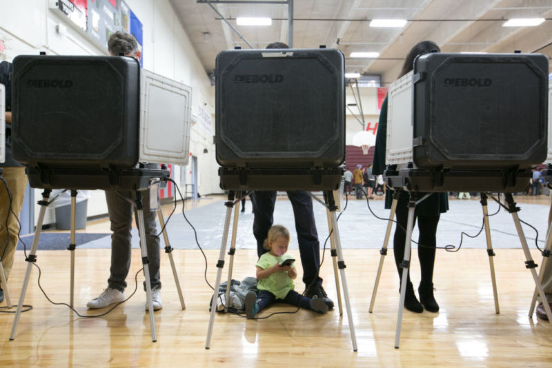 ATLANTA, GA - NOVEMBER 06: Sloane (no last name given), 2, waits between her father's legs as he and other voters cast their ballots at a polling station set up at Grady High School for the mid-term elections on November 6, 2018 in Atlanta, Georgia. Georgia has a tight race to elect the state's next governor and a lot of worries over voting security. (Photo by Jessica McGowan/Getty Images)