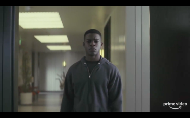 A man stands blankly in an institutional corridor.