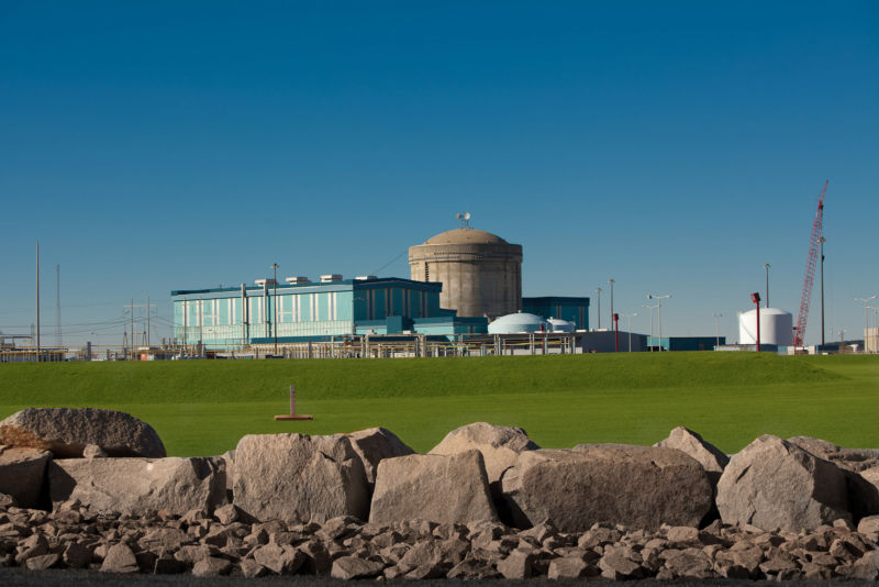 A nuclear power plant in a grass field during the summer.