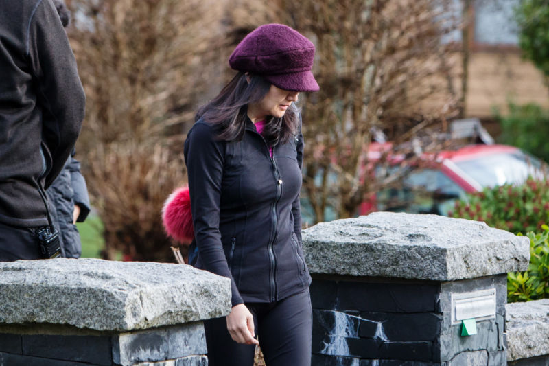 A woman walks toward a sidewalk while a hat obscures part of her face.