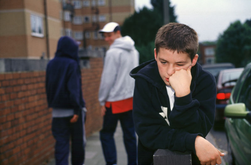 A boy looks sad while other, out-of-focus boys appear to laugh at him.