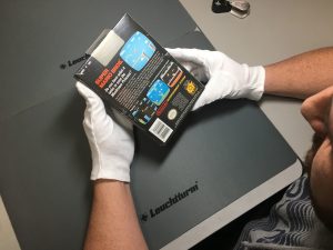 A man in white gloves examines a boxed NES game.