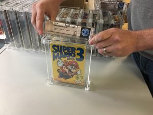 Two hands seal a boxed NES game into a clear container.